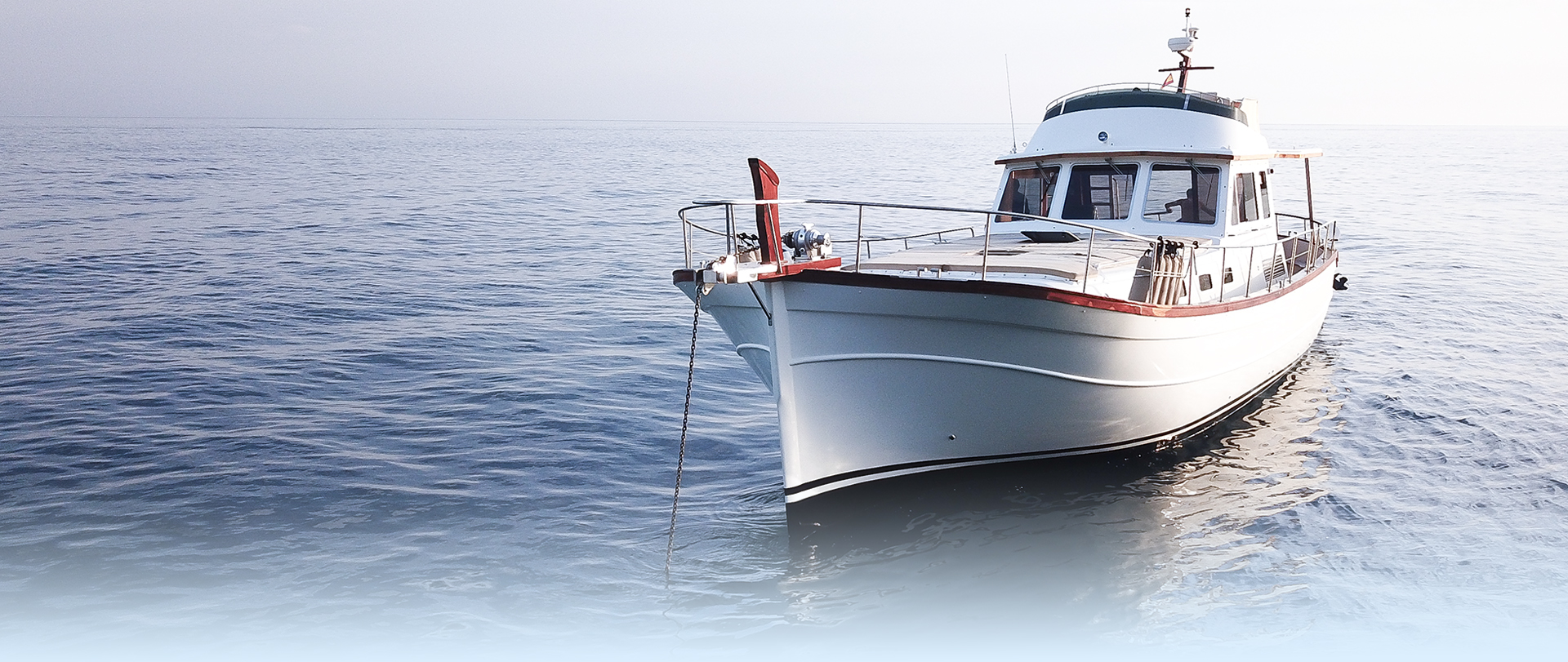 Gorgeous white and teak wooden boat tied to a montage buoy at sunrise on a calm morning with a blurred reflection and a cloudy backdrop.