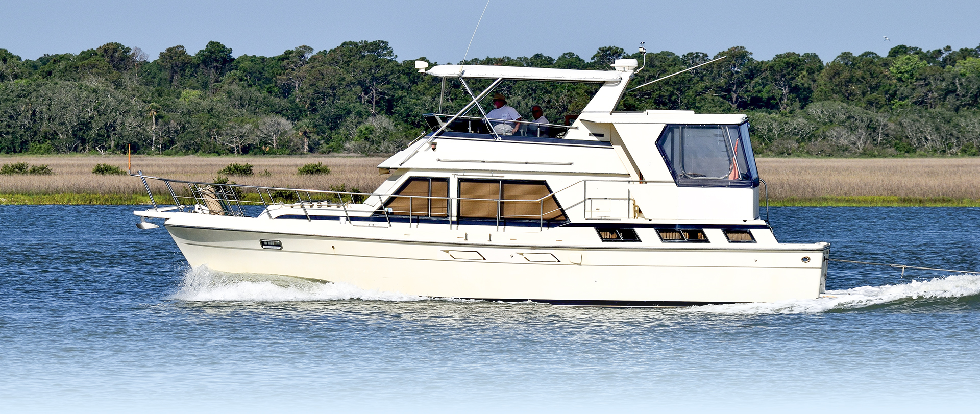 Gorgeous white and teak wooden boat tied to a montage buoy at sunrise on a calm morning with a blurred reflection and a cloudy backdrop.